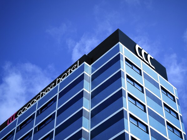 A modern hotel building with a prominent 'Cocoach Hotel' sign, featuring a geometric facade and multiple balconies.