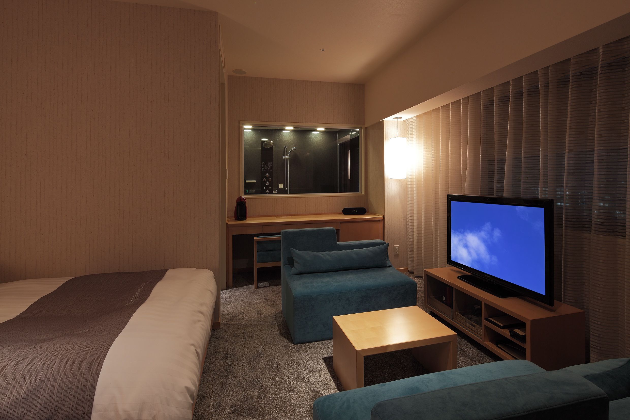 A hotel room with a bed, a desk, a television, and a seating area.