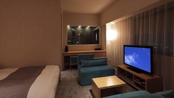 A hotel room with a bed, a desk, a television, and a seating area.