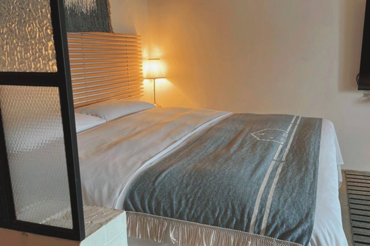 A hotel room with a bed, a bedside lamp, and a TV mounted on the wall.