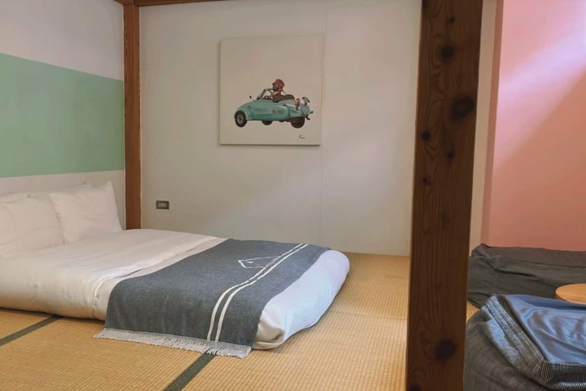 A single bed with a grey and white blanket, a framed picture on the wall, and a wooden headboard.