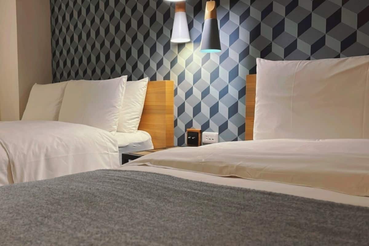 A hotel room with two beds, a patterned wall, and a nightstand with a lamp.