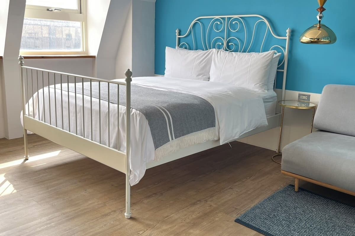 A room with a white metal bed, a blue accent wall, a small round table, and a grey armchair.