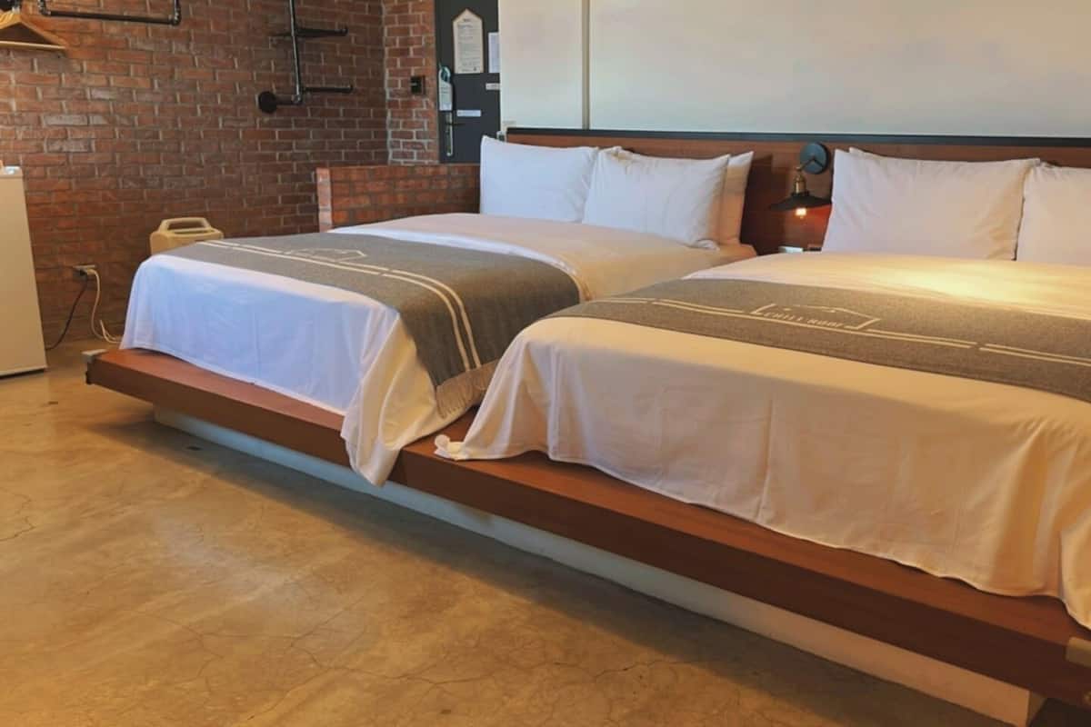A hotel room with two beds, a brick wall, and a wooden floor.
