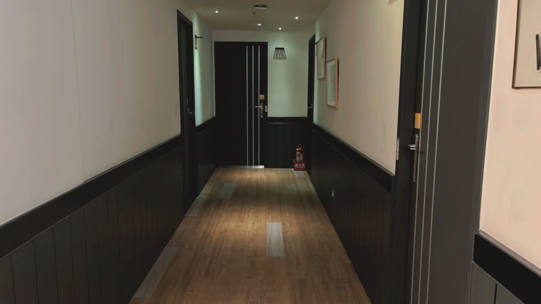 Un pasillo con suelo de madera, paredes oscuras y una puerta al final.