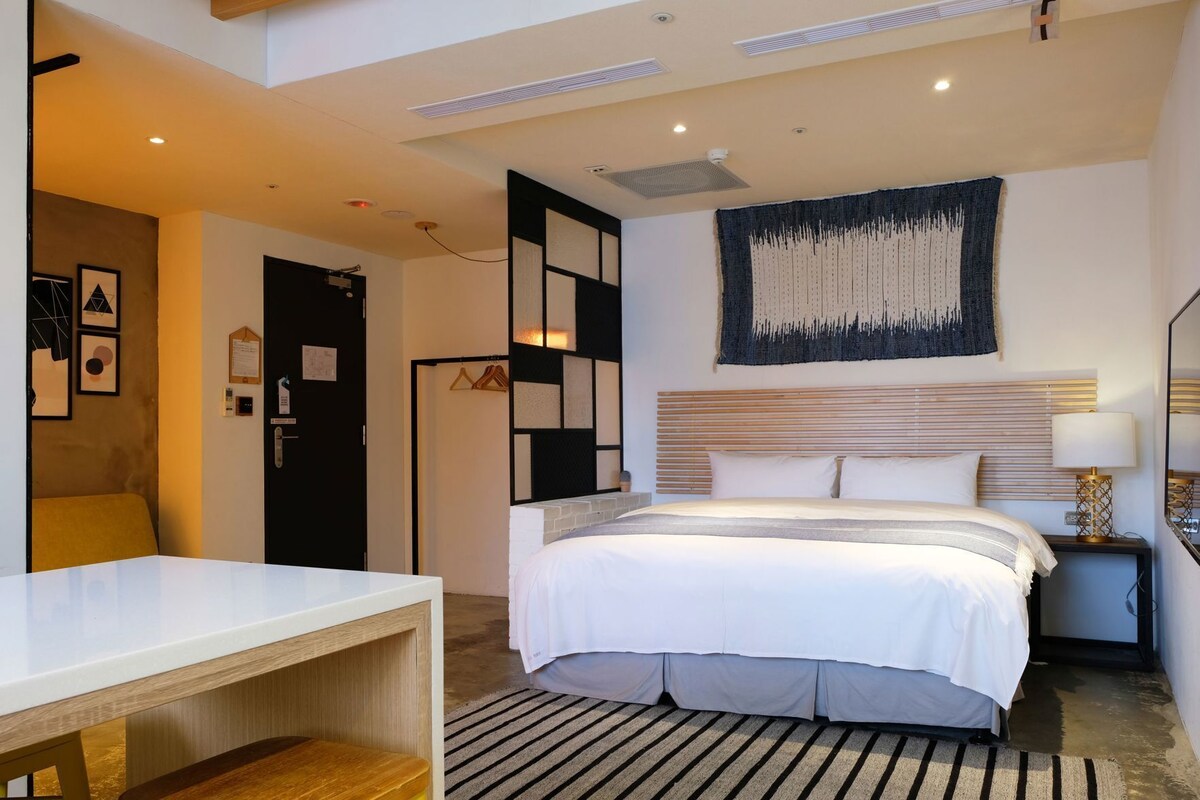 A hotel room with a bed, bedside table, lamp, and a wall-mounted artwork.