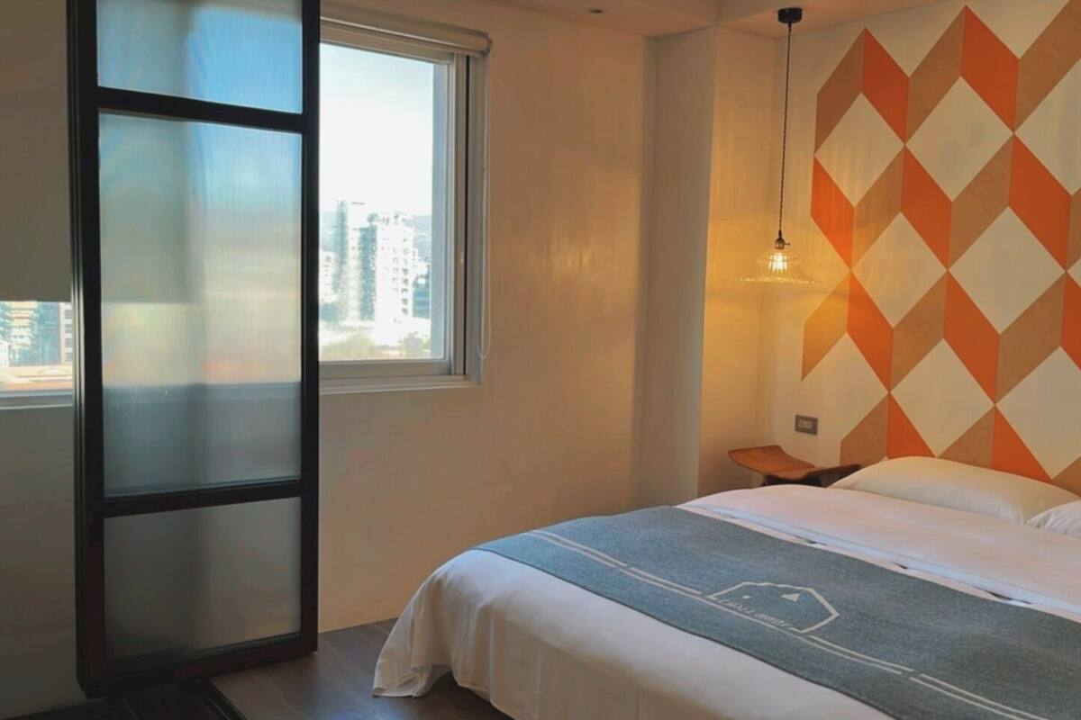 A hotel room with a bed, a window, and a wall with a geometric pattern.