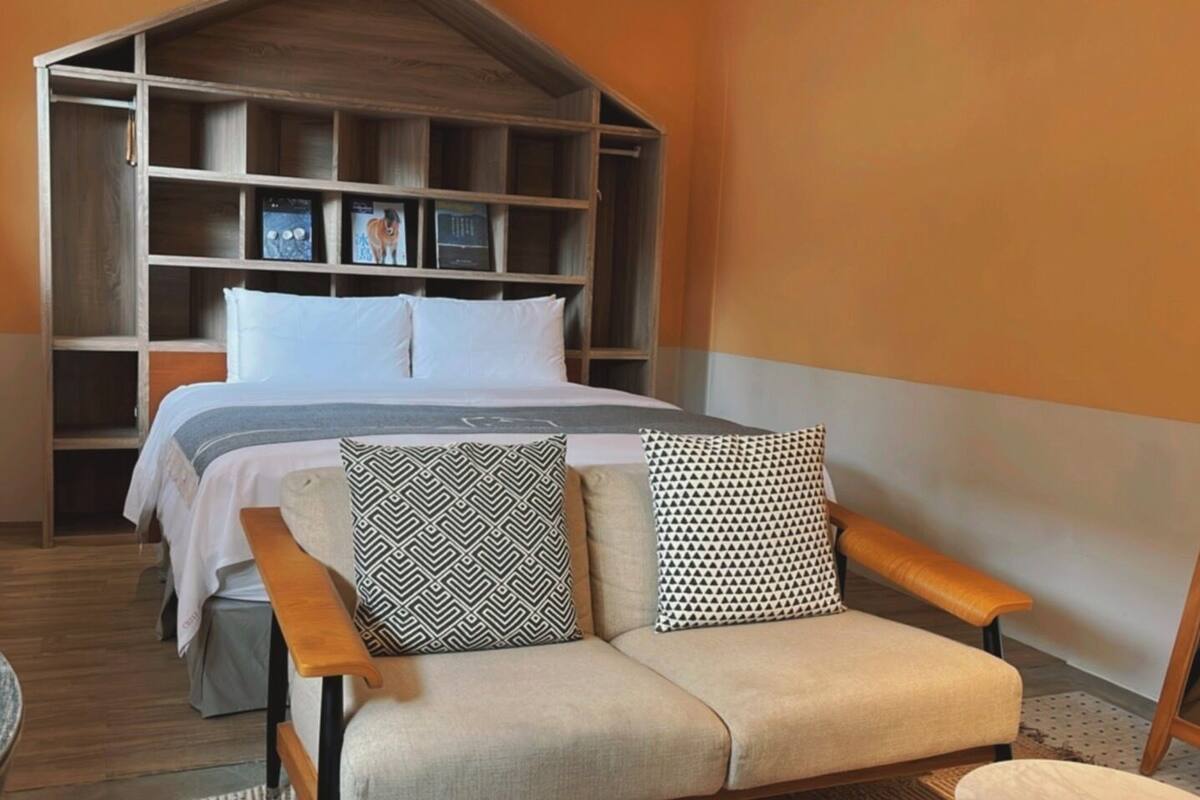 A bedroom with a bed, a wooden wardrobe, a sofa with patterned cushions, and a wooden bench.
