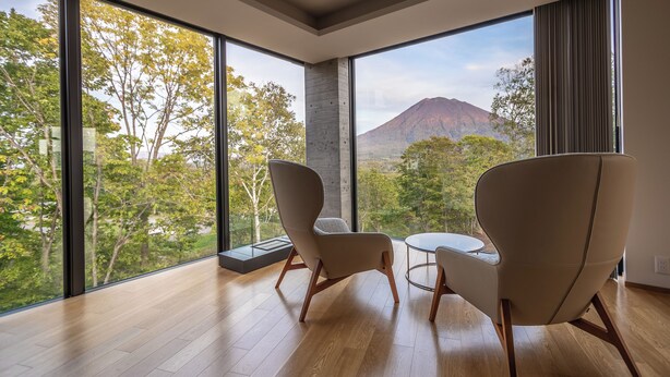 A modern room with large windows, two chairs, a small table, and a view of a mountain. - Kozue (Kutchan)