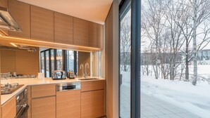 A modern kitchen with wooden cabinets, stainless steel appliances, and a large window overlooking a snowy outdoor area. - Kozue (Kutchan)