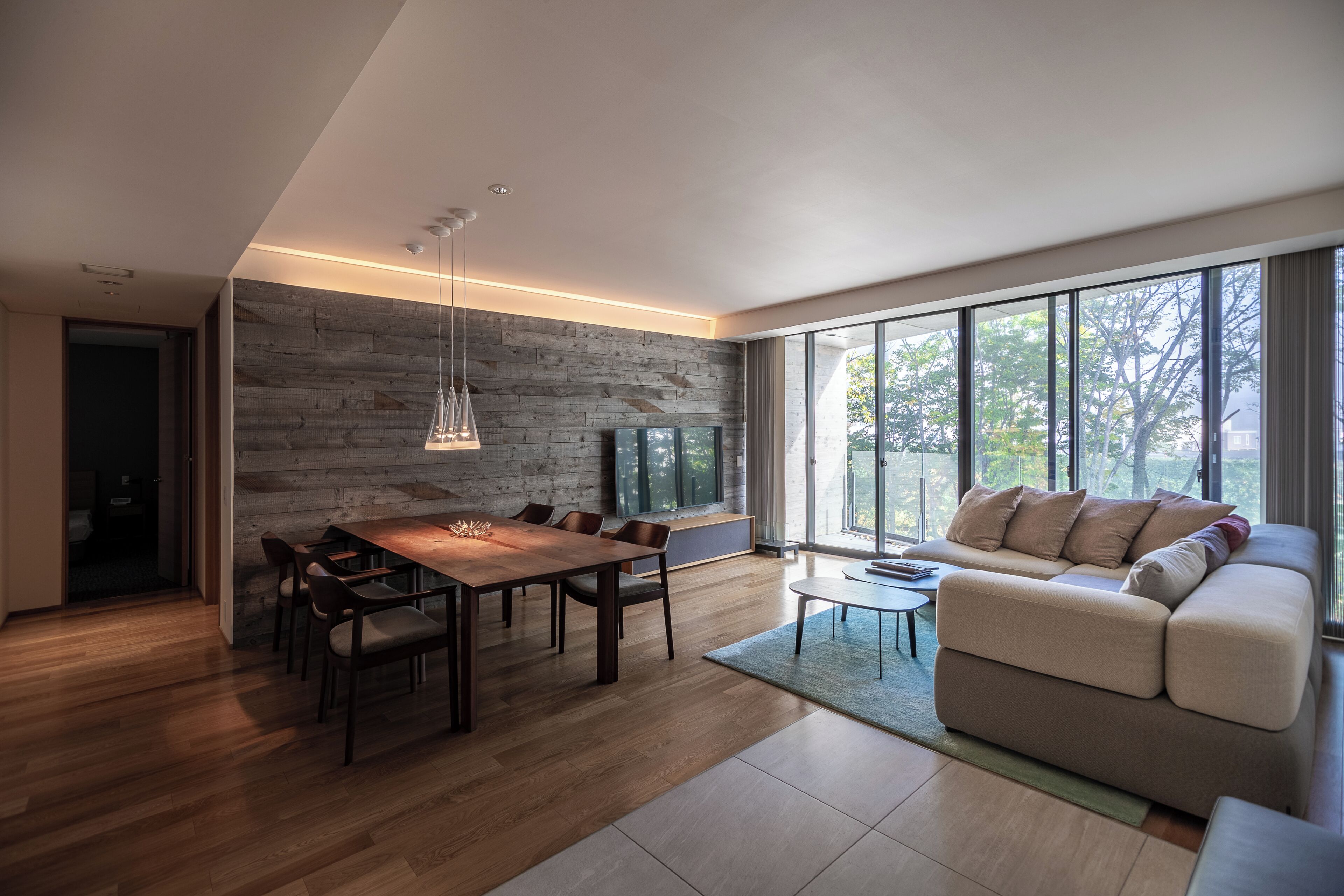 A modern living room with a wooden dining table, a sofa, and a TV against a stone wall.
