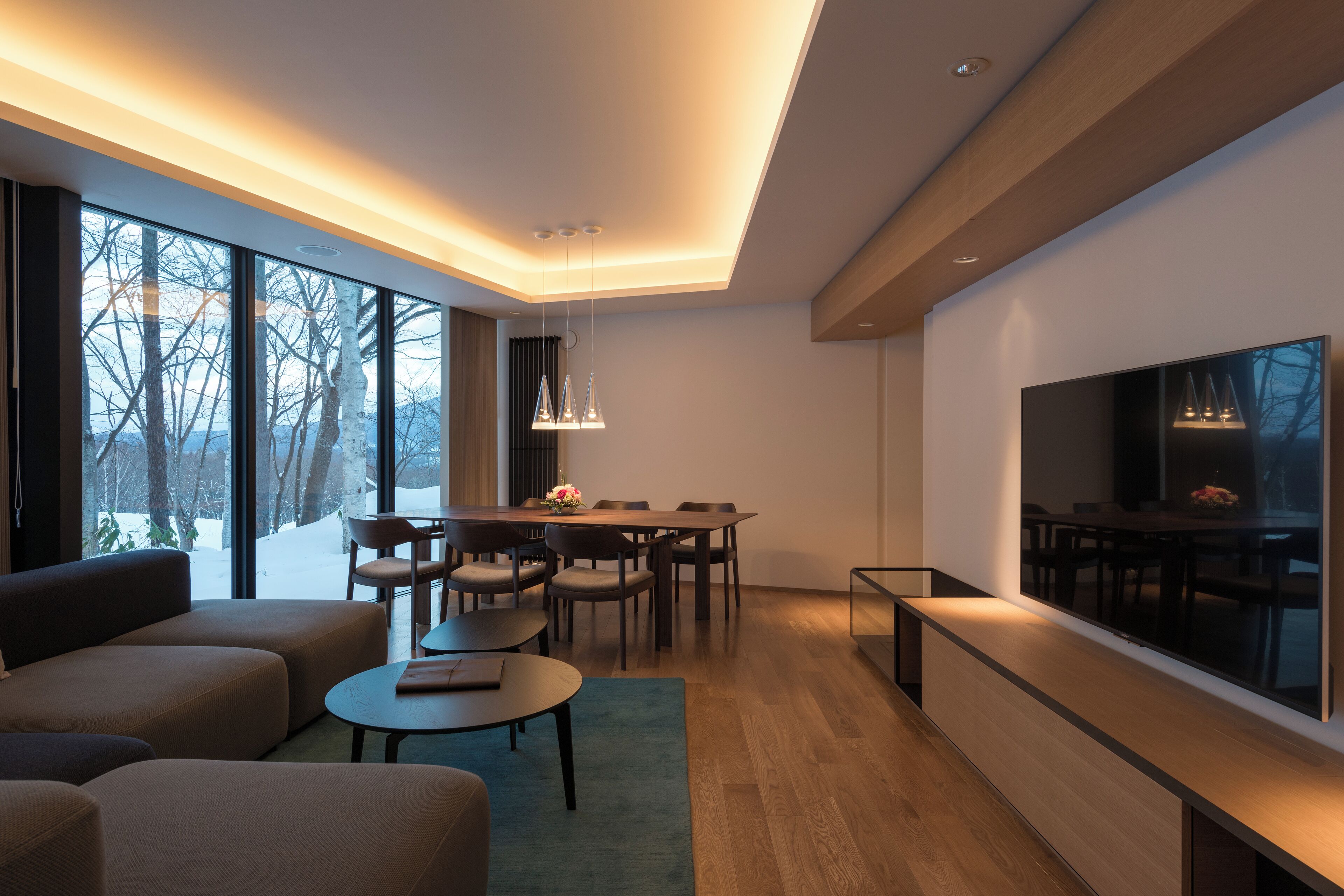 Un salon moderne doté d’un grand téléviseur, d’un plancher en bois et d’un coin repas avec une table et des chaises.