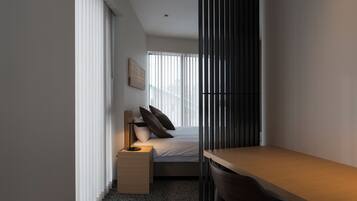 A compact hotel room with a bed, a desk, a chair, and a nightstand.