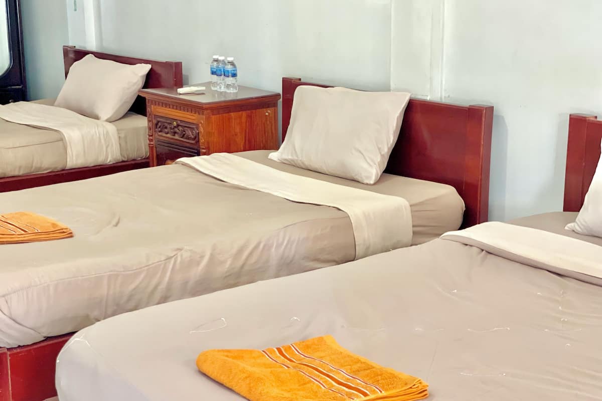 A hotel room with two beds, each with a beige bedspread and pillows, and a wooden nightstand with a water bottle.