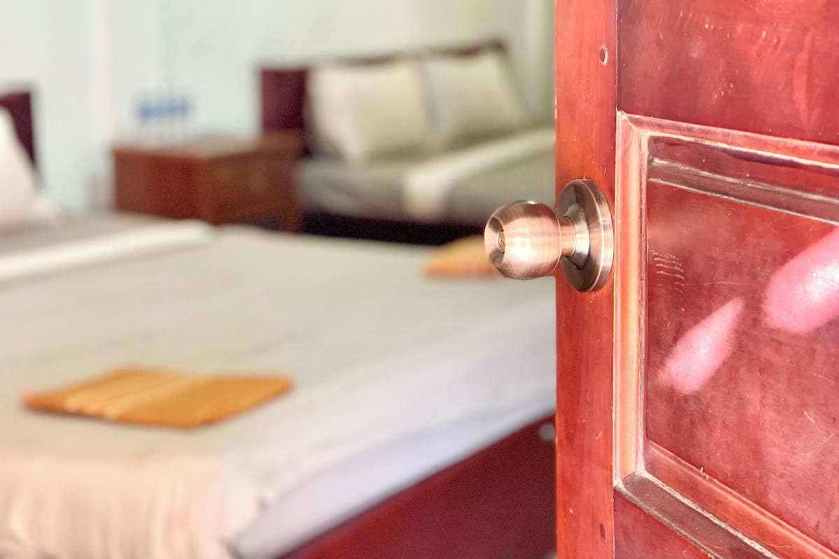 A wooden door with a round knob, leading to a room with a bed, pillows, and a nightstand.