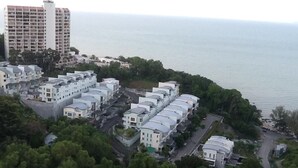 A coastal residential area with modern apartment buildings, a road, and dense greenery.