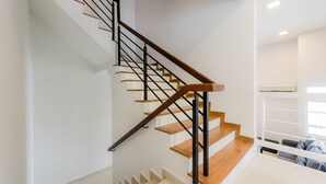 A modern staircase with wooden steps and black metal railings, leading to a bright room with white walls and a ceiling light.