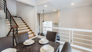 A modern dining area with a staircase, a dining table set with plates and cutlery, and a view of the kitchen in the background.