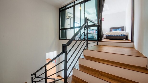 A staircase with wooden steps and black railings leading to a room with a bed and a window.