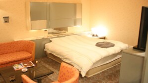 A hotel room with a bed, a chair, a small table, a mirror, and a television.