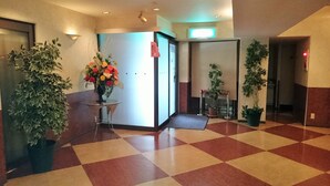 A hotel lobby with a checkered floor, a reception desk with a vase of flowers, and potted plants.
