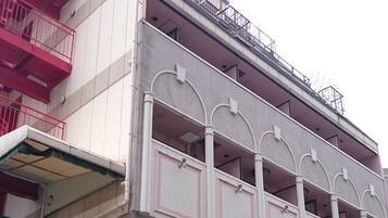 A multi-story building with a prominent 'Alpina' sign on the ground floor, a balcony with railings, and a parking sign.