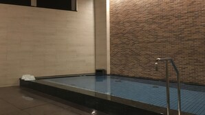 Una piscina con piso de baldosas, pared de ladrillo y techo de madera.