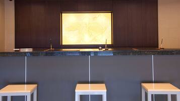 Un área de recepción con un panel de madera oscura, una mesa de recepción y tres taburetes blancos.
