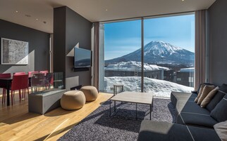 Un salon moderne doté d’une grande fenêtre, d’un téléviseur à écran plat, d’un canapé et d’un coin repas avec des chaises rouges.