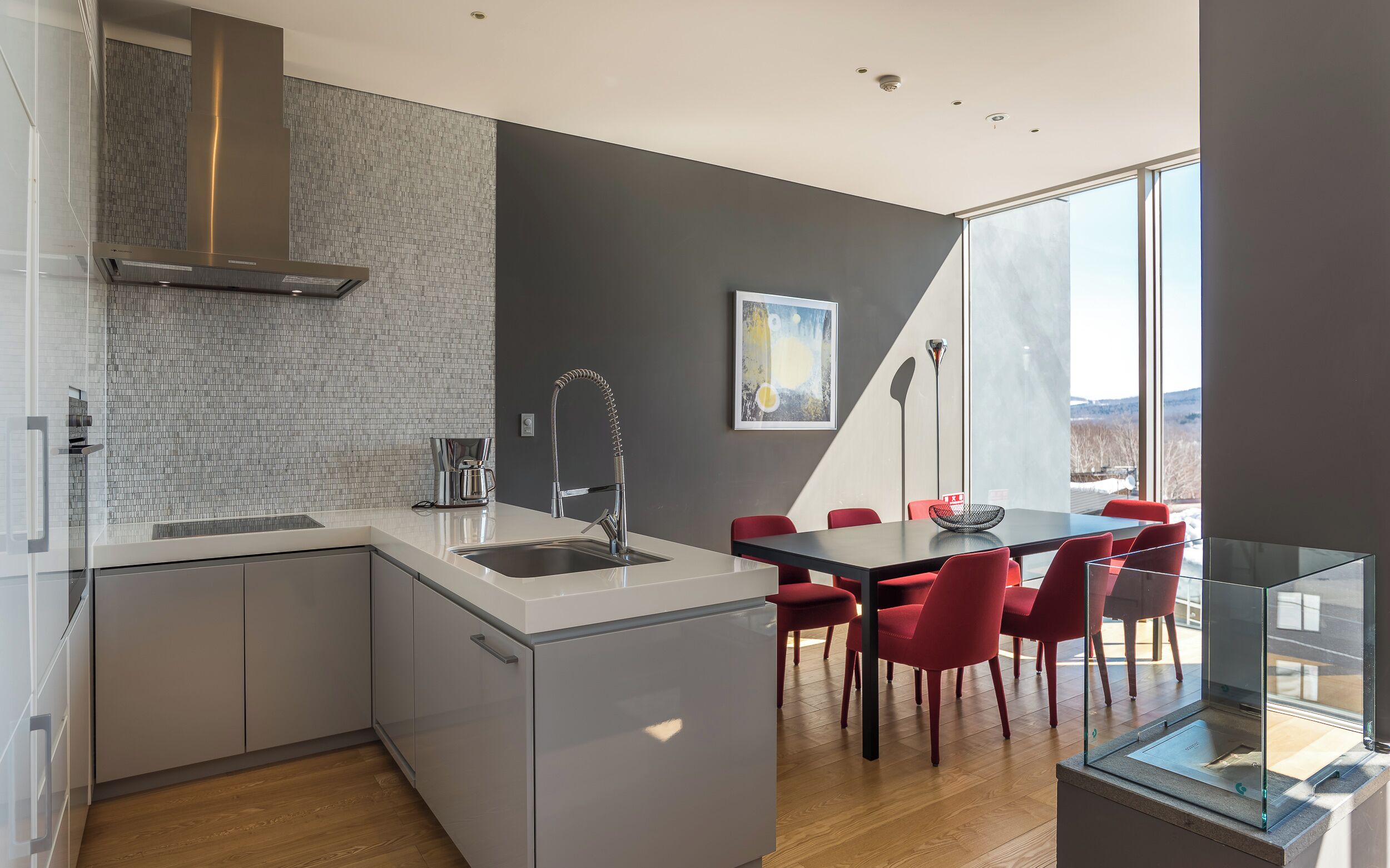 A modern kitchen with a large island, a dining area with red chairs, and a view of the outdoors.
