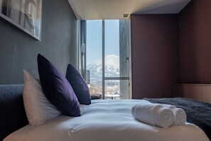 A hotel room with a large window, a bed with white linens, and a view of a mountain. - Terrazze Niseko (Kutchan)