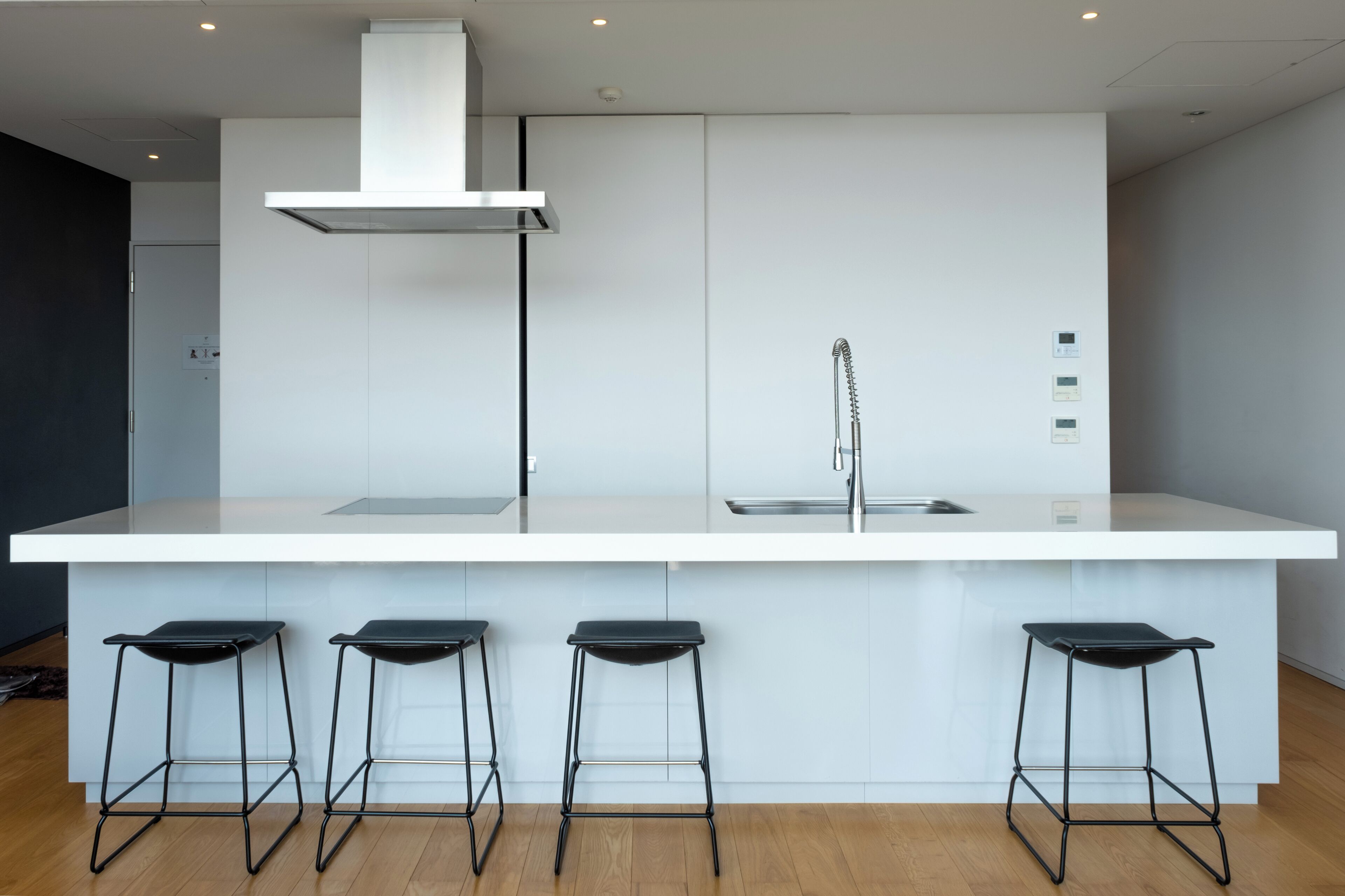 Une cuisine moderne avec un plan de travail blanc, un évier en acier inoxydable et trois tabourets de bar noirs.