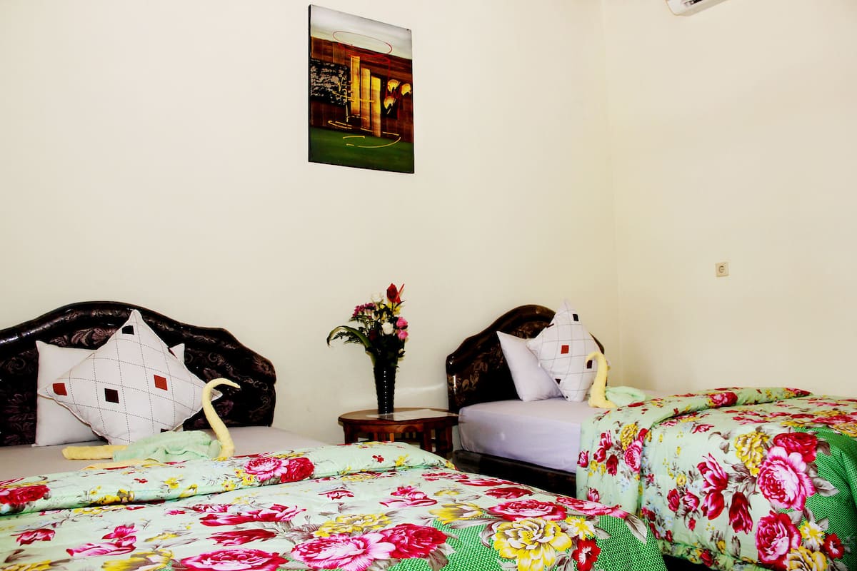 A bedroom with two beds, a nightstand, a vase with flowers, and a painting on the wall.
