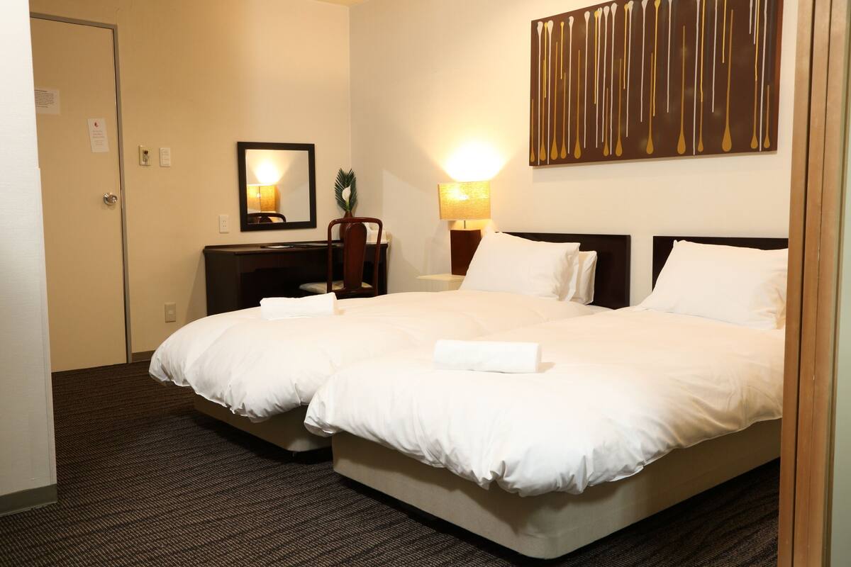 A hotel room with a double bed, a desk with a chair, a lamp, and a mirror on the wall.