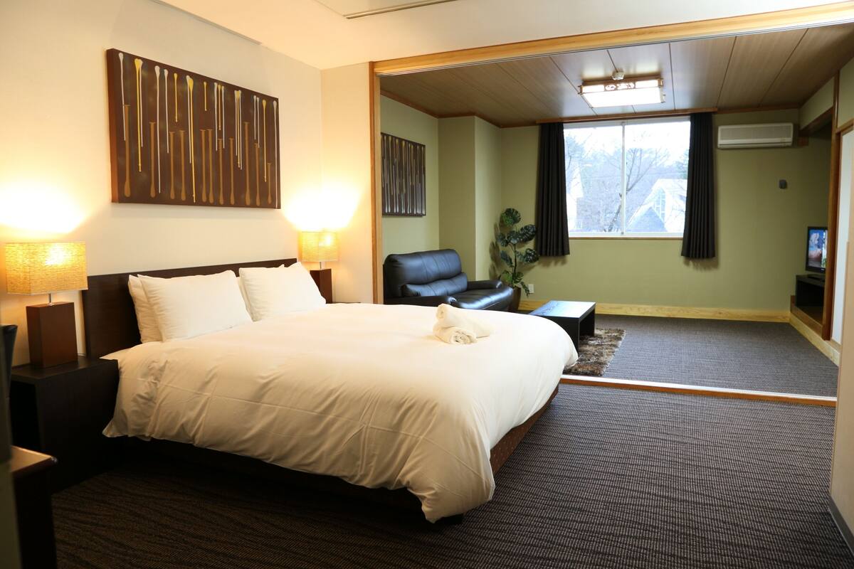 A hotel room with a large bed, two bedside lamps, a leather chair, a small table, and a TV.