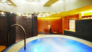 A modern indoor pool with a clear water surface, surrounded by a tiled wall and a seating area with chairs and a small table. - The T Hotel (Hong Kong)
