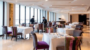 A spacious dining area with tables set for service, large windows, and a modern ceiling design. - The T Hotel (Hong Kong)