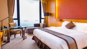 A hotel room with a large bed, a desk with a chair, a sofa, and a view of the sea through large windows. - The T Hotel (Hong Kong)