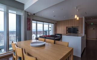 Un espacio habitable moderno con comedor, sofá, televisor y ventanas amplias con vistas a las montañas.