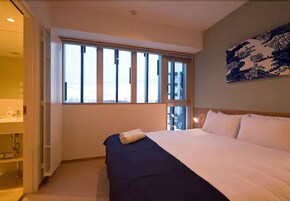Une chambre d’hôtel avec un grand lit, une fenêtre avec des stores, une table de chevet et une œuvre d’art accrochée au mur.