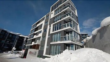 Un immeuble à plusieurs étages, doté de balcons, de grandes fenêtres et dont le sol est recouvert de neige.