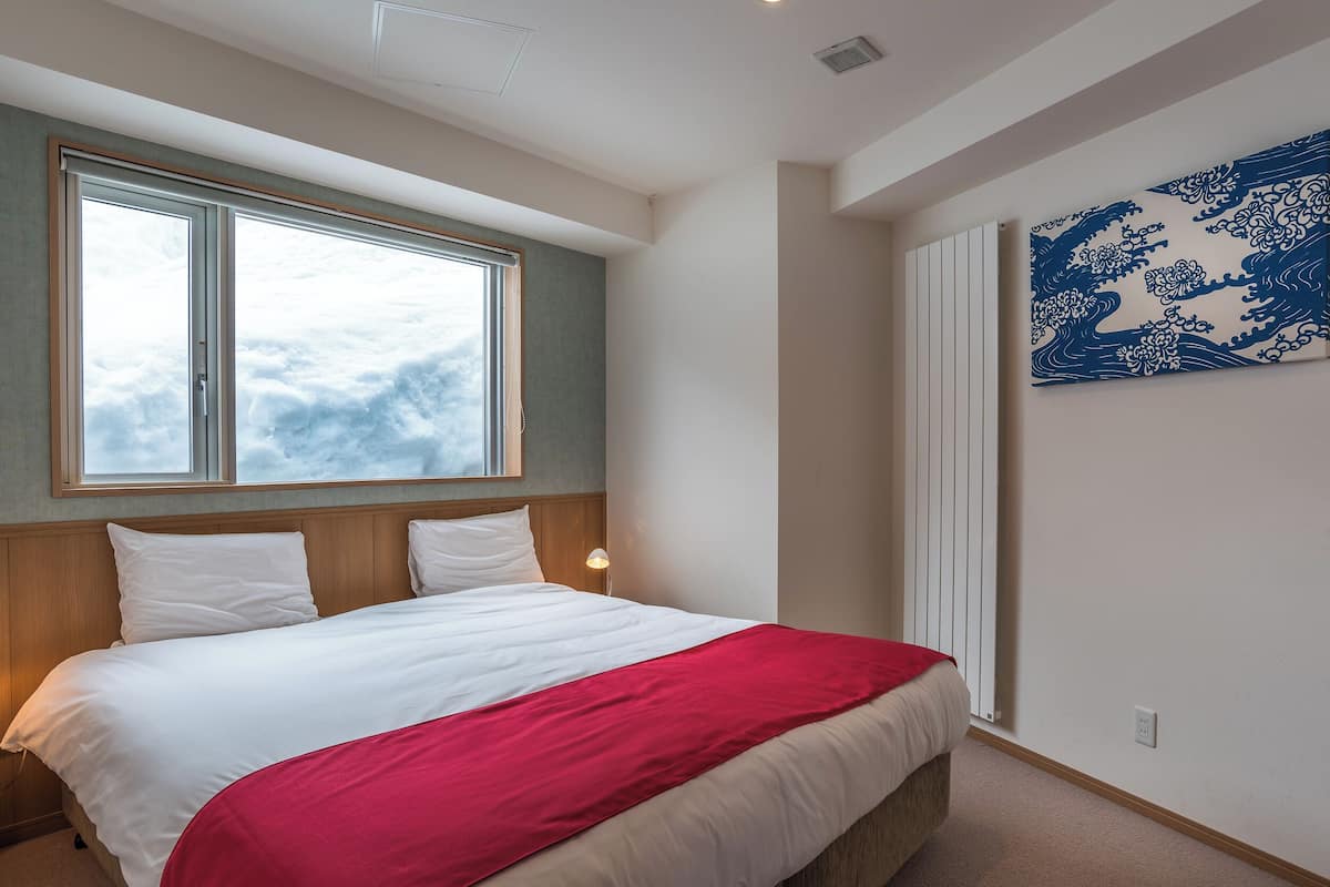 Ein Schlafzimmer mit einem großen Bett, einem Fenster mit Blick auf Wolken und einer Wand mit blau-weißem Muster.