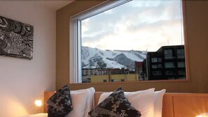 A hotel room with a bed, two pillows, a window with a view of snow-covered mountains, and a wall art piece. - Snow Crystal (Kutchan)