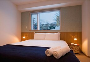 Une chambre d’hôtel avec un grand lit, une fenêtre donnant sur un paysage enneigé et une table de chevet avec une lampe.