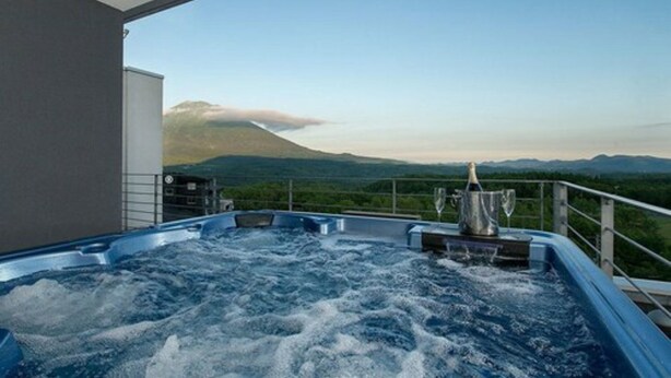 A hot tub with a mountain view, a champagne bottle, and glasses on a balcony. - Snow Crystal (Kutchan)