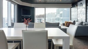 Una sala de estar moderna con una mesa de comedor blanca, sofás grises y un ventanal con vistas a la ciudad.