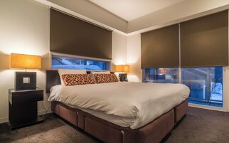 Ein modernes Hotelzimmer mit einem großen Bett, zwei Nachttischen mit Lampen und Blick auf eine verschneite Landschaft durch die Fenster.