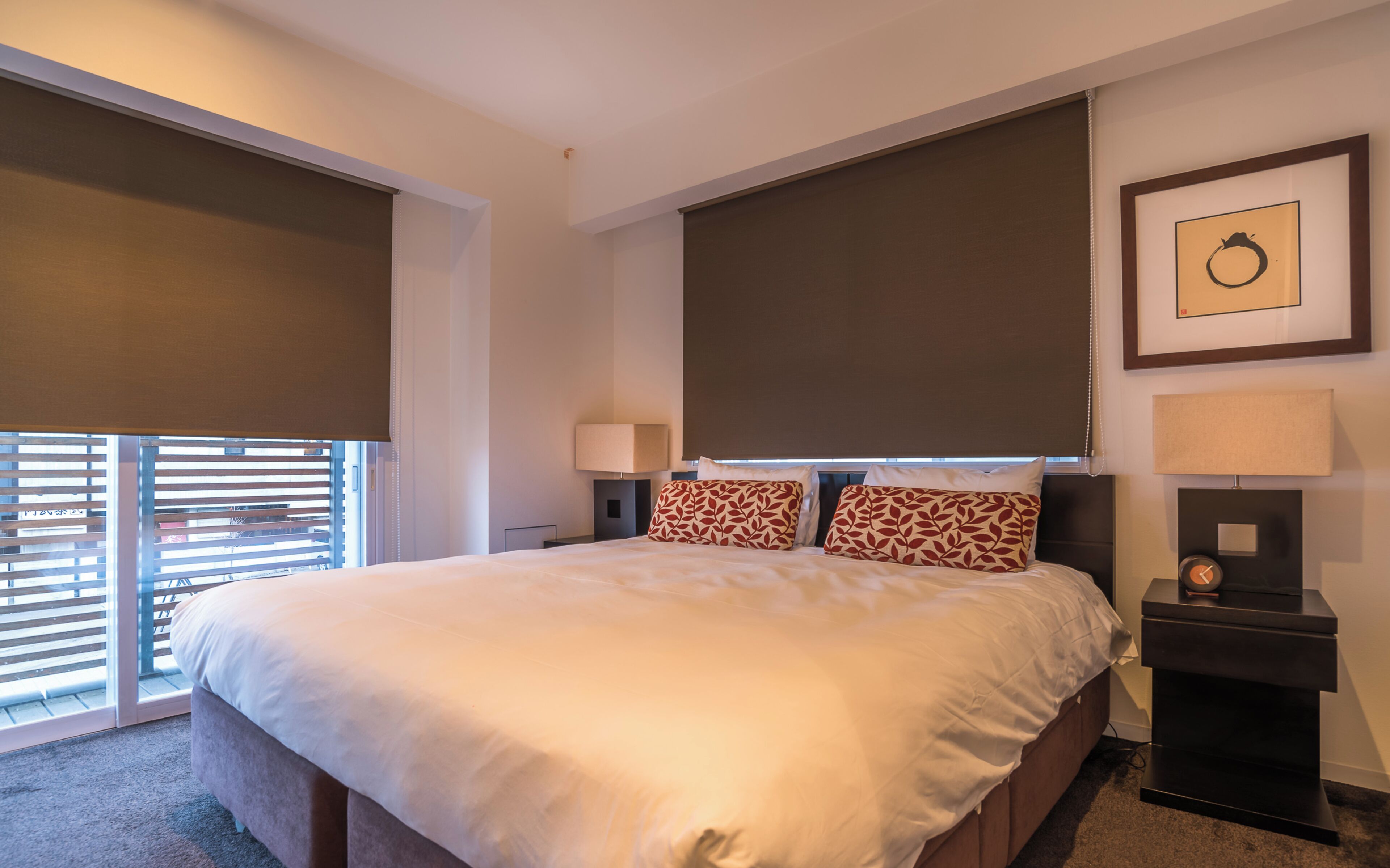 A hotel room with a large bed, two bedside lamps, a clock, and a framed picture on the wall.