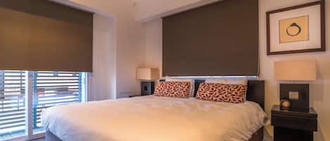 A hotel room with a large bed, two bedside lamps, a clock, and a framed picture on the wall.