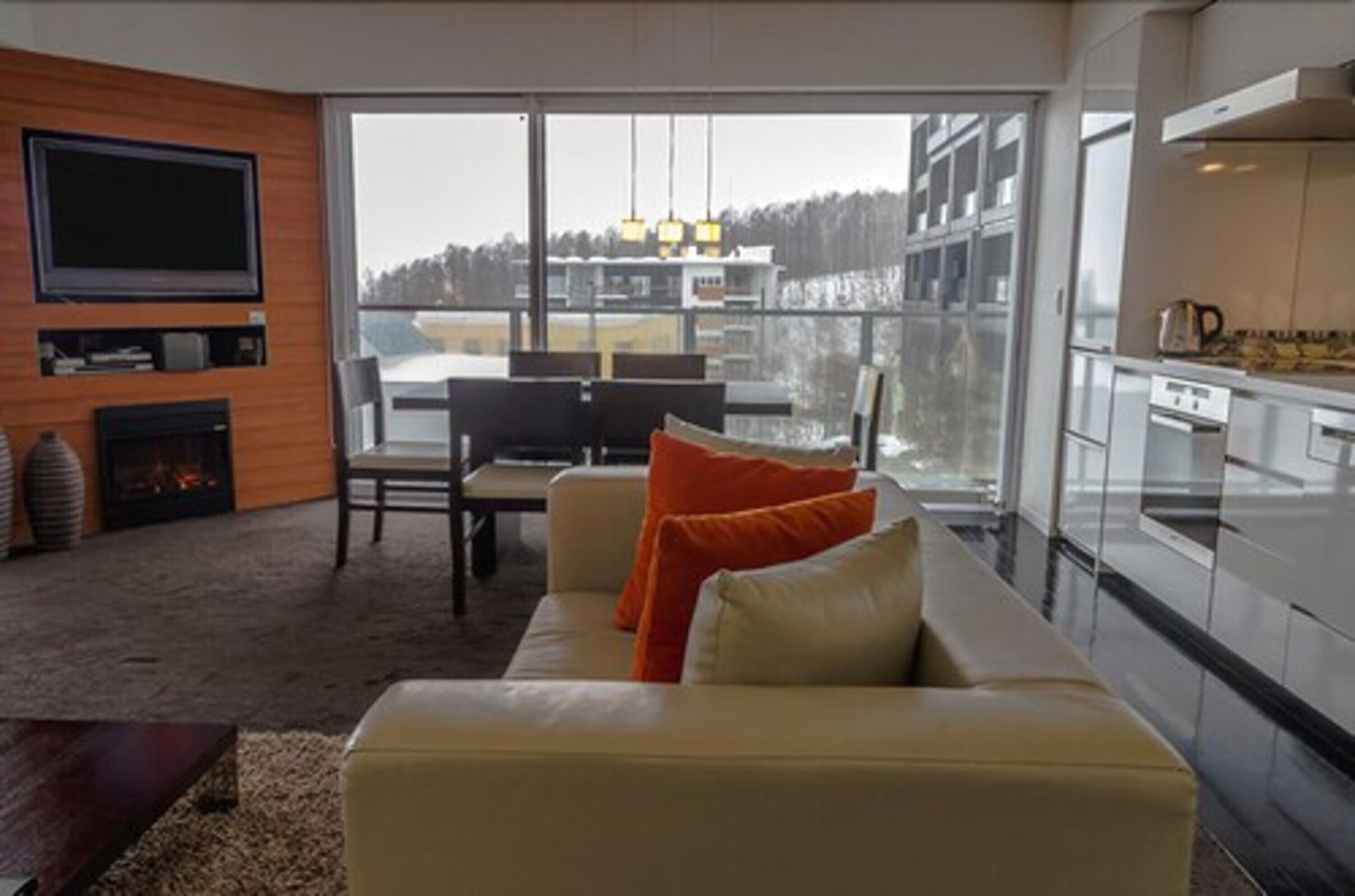 A modern living room with a sofa, television, fireplace, and large windows overlooking a cityscape.